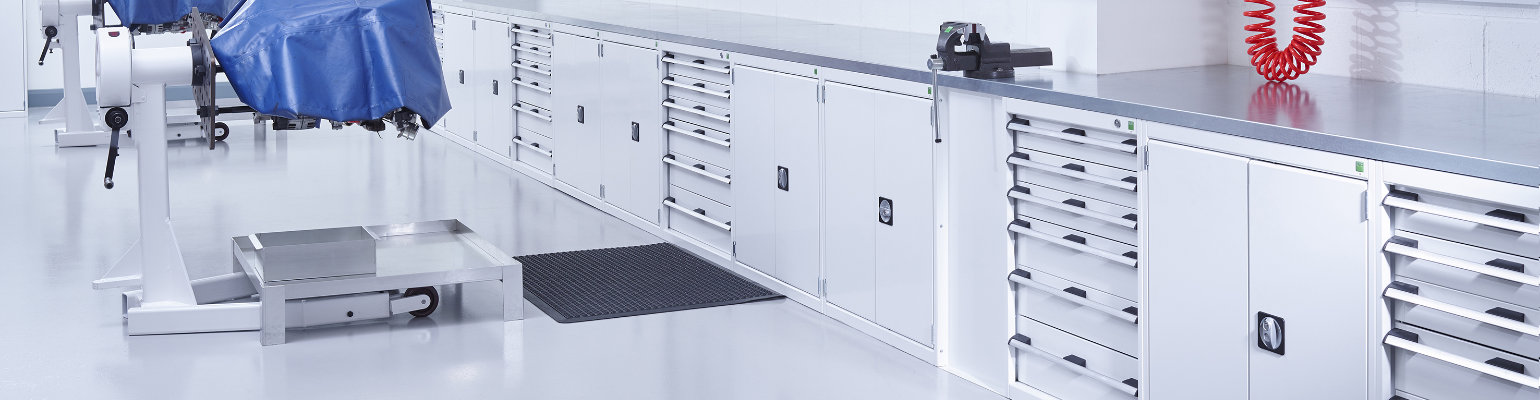 A long row of low cubio cabinets with worktops and back panels in an automotive workshop.